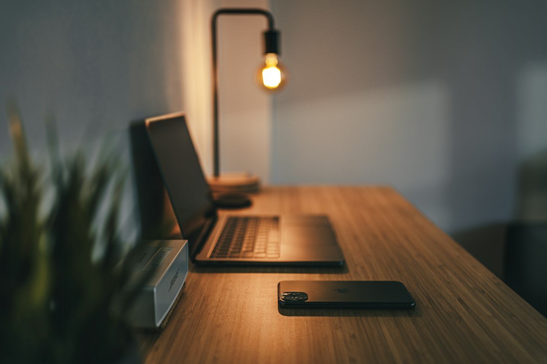 Laptop, phone and lamp on a wooden desk, suggesting accounting work on mobile and desktop.